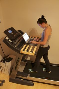 a woman using a laptop on top of a treadmill in a room with hard wood flooring