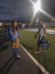 a man and woman standing on a soccer field at night with the lights turned on