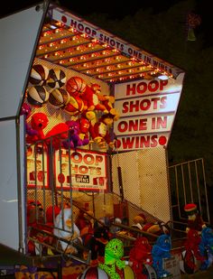 a carnival booth with lots of stuffed animals on it's sides and lights hanging from the roof