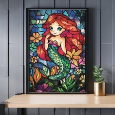 a stained glass window with a little mermaid sitting on it's side, next to a potted plant