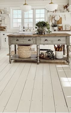 a kitchen with white walls and wooden floors is pictured in this image, there are plants on the island