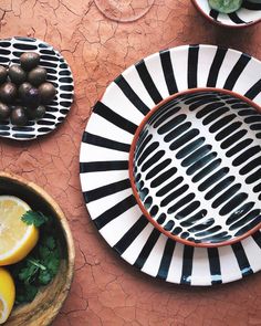 plates with black and white designs sit on a table next to bowls filled with fruit