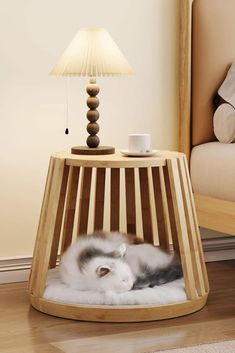 a cat sleeping in a wooden cage on the floor next to a lamp and bed