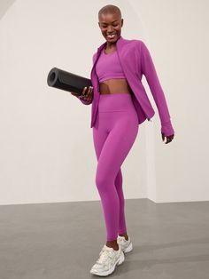 a woman in a purple outfit holding a black object while standing on a gray floor