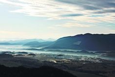 the mountains are covered in fog and clouds as seen from atop a mountaintop at dusk