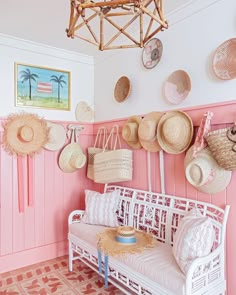 a pink room with hats hanging on the wall and a white bench in front of it