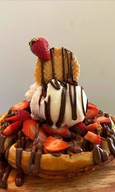 a waffle topped with ice cream, strawberries and chocolate sauce on a wooden platter