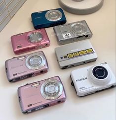 several cameras sitting on top of a table next to each other, all in different colors