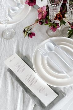 the table is set with white plates, silverware and purple flowers in vases