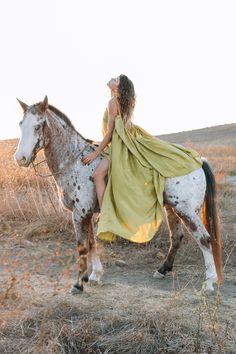 a woman in a yellow dress is riding a brown and white horse through the field