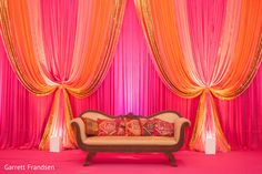 a couch sitting in front of pink drapes and orange pillows on top of it