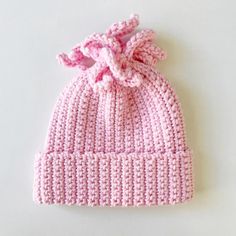 a pink knitted hat with a knot on the front and side, sitting on a white surface