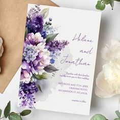 a wedding card with purple flowers and greenery on it, next to a flower bouquet