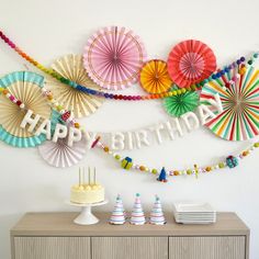 a birthday party with colorful paper fans and streamers hanging on the wall above it