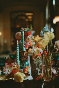 a table topped with lots of vases filled with flowers next to tall blue candles