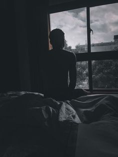 a person sitting on a bed in front of a window looking out at the city