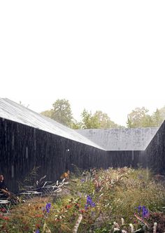 two people sitting in the rain at an open air structure with plants and flowers around them