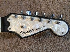 a white and black electric guitar laying on top of a carpeted floor with the words fender stratner written on it