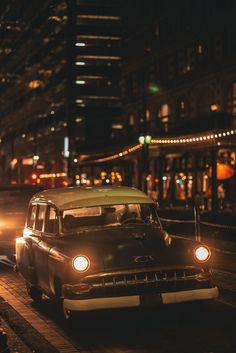 an old car is driving down the street in the city at night with its lights on