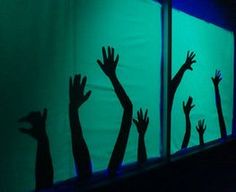 silhouettes of hands reaching up into the air in front of a green screen with blue lights