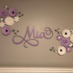 the name made out of paper flowers is displayed in front of a gray wall with white and purple flowers