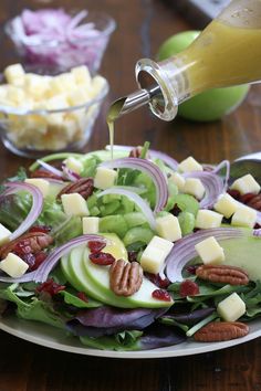 a salad with apples, lettuce and pecans is being drizzled with dressing