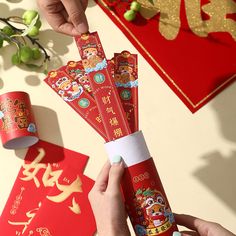 someone is holding up red packets with chinese writing on them and two hands are reaching for one