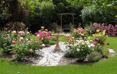 a garden filled with lots of flowers next to a stone path and bench in the middle