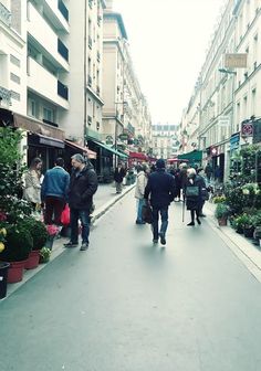 people are walking down the street in an urban area with many plants and flowers on display