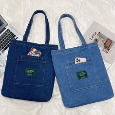 two denim bags sitting on top of a bed next to an open laptop and magazine