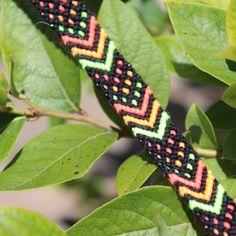 a colorful beaded bracelet sitting on top of a green leaf covered tree branch with leaves around it