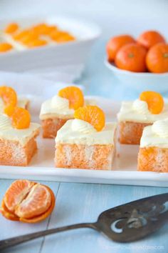 several pieces of cake on a white plate with oranges in the bowl behind it