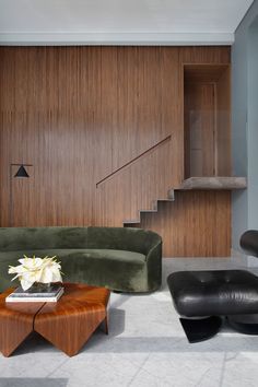 a modern living room with green velvet couches and black leather foot stools in front of a wood paneled wall