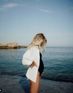 a woman in a black and white one piece swimsuit standing on the beach with her back to the camera