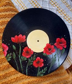 a black record with red flowers painted on it sitting on top of a yellow blanket