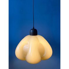 a yellow light hanging from a black cord on a blue wall with an object in the background