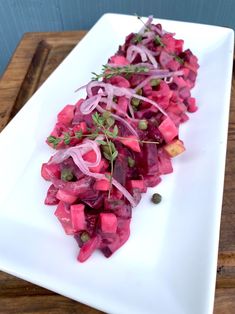 a white plate topped with beets and onions on top of a wooden cutting board