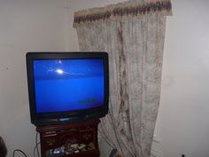 a television sitting on top of a wooden stand in front of a curtained window