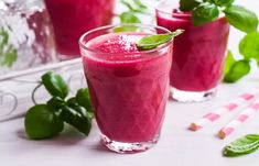 two glasses filled with pink smoothie and garnished with green leafy leaves