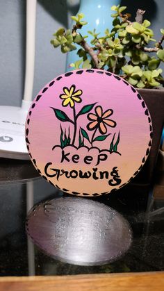 a wooden sign that says keep growing with flowers in the center on a table next to a potted plant