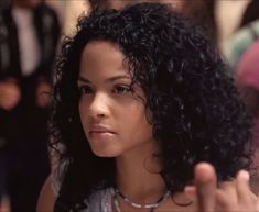 a close up of a woman with curly hair pointing to the side while wearing a necklace