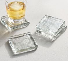 three square glass coasters with ice cubes on the bottom and one filled with liquid