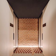 an empty hallway with red and white tiles on the wall, leading to another room