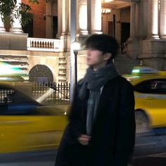 a young man walking down the street in front of some taxi cabs at night