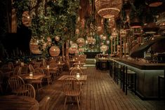 a restaurant with wooden tables and chairs covered in hanging lights, plants and lanterns on the ceiling