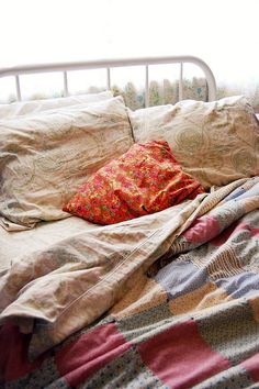 an unmade bed with many pillows and blankets on it, in front of a window