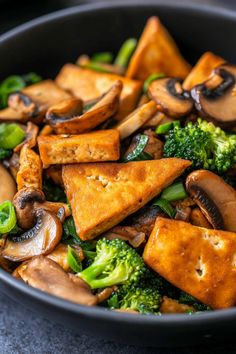 a pan filled with tofu, broccoli and mushrooms on top of a table