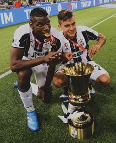 two soccer players kneeling next to a trophy