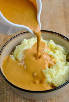 a bowl filled with mashed potatoes and gravy being poured into the bowl