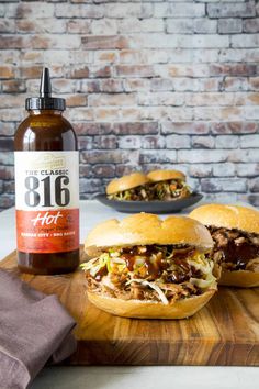 bbq pulled pork sandwiches on a cutting board next to a bottle of hot sauce